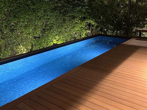 Blue liner pool with a timber deck at night